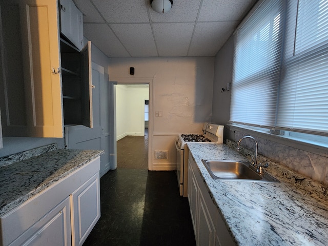 kitchen featuring light stone counters, a drop ceiling, gas range gas stove, sink, and white cabinets