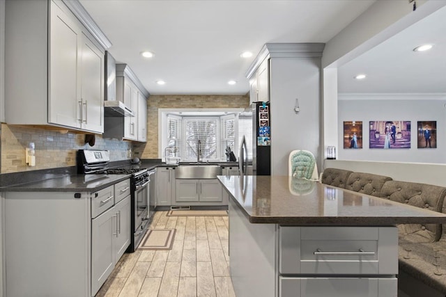 kitchen with gray cabinets, appliances with stainless steel finishes, tasteful backsplash, wall chimney range hood, and sink