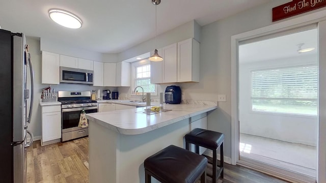 kitchen featuring white cabinetry, kitchen peninsula, pendant lighting, a breakfast bar area, and appliances with stainless steel finishes