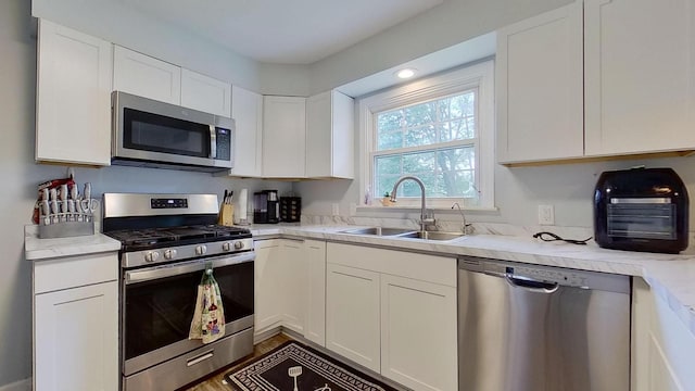 kitchen with light stone countertops, dark hardwood / wood-style flooring, stainless steel appliances, sink, and white cabinets