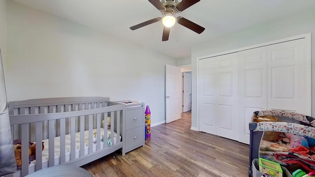 bedroom with hardwood / wood-style flooring, ceiling fan, a crib, and a closet