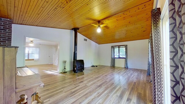 unfurnished living room featuring lofted ceiling, wood ceiling, a wood stove, ceiling fan, and light hardwood / wood-style floors