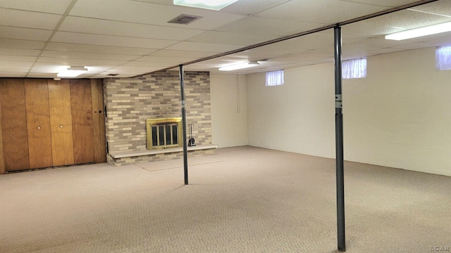 basement with wooden walls, a fireplace, light colored carpet, and a drop ceiling