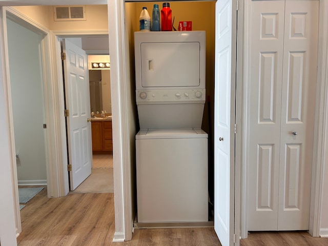 laundry area featuring sink, stacked washer and clothes dryer, and light hardwood / wood-style flooring