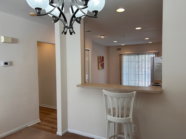 kitchen featuring a kitchen bar, an inviting chandelier, fridge, dark carpet, and kitchen peninsula