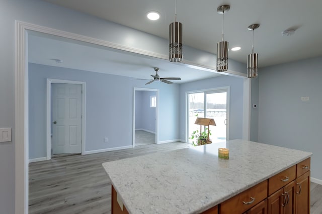 kitchen featuring decorative light fixtures, a center island, ceiling fan, light stone counters, and light hardwood / wood-style floors