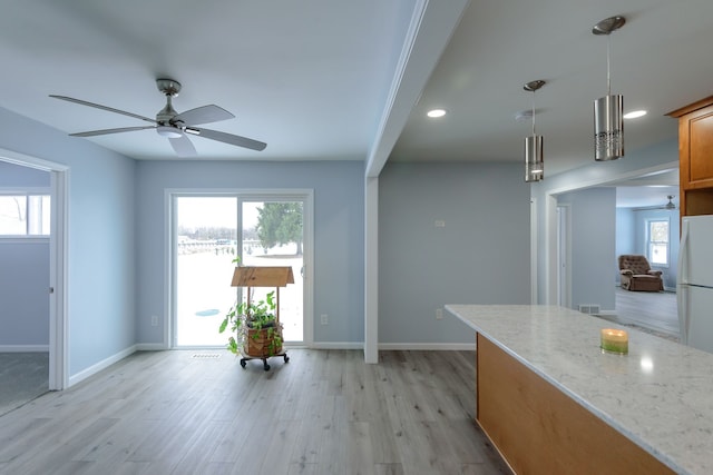 kitchen featuring pendant lighting, a wealth of natural light, light stone countertops, and white fridge