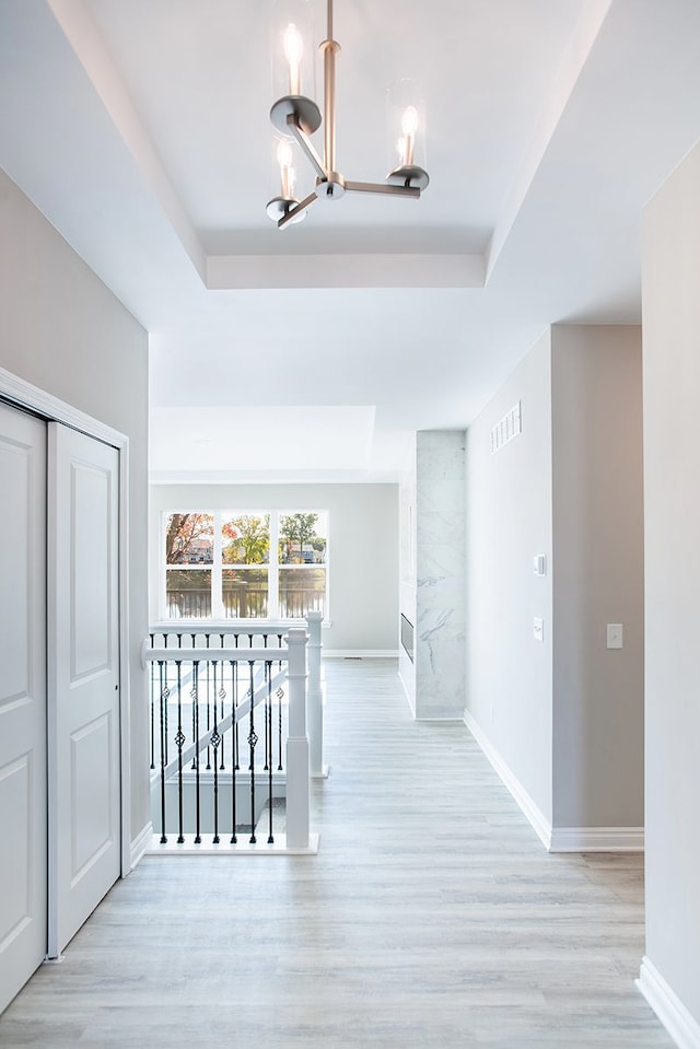 corridor with a raised ceiling, light hardwood / wood-style floors, and a chandelier