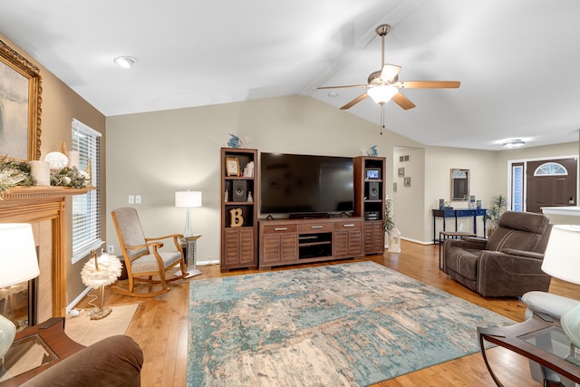 living room with ceiling fan, light wood-type flooring, vaulted ceiling, and a fireplace