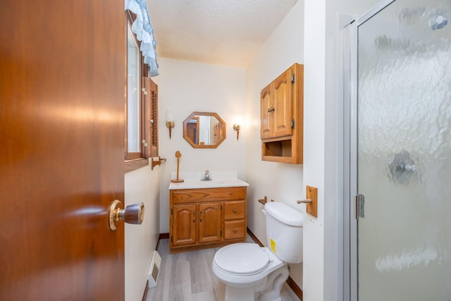 bathroom with vanity, toilet, a textured ceiling, an enclosed shower, and wood-type flooring