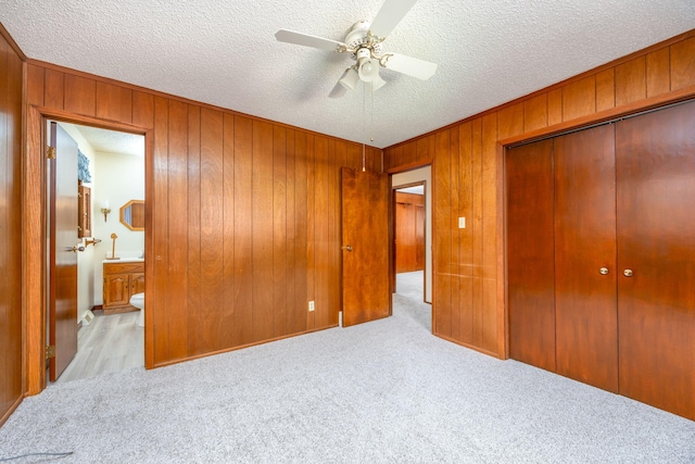 unfurnished bedroom with ensuite bath, ceiling fan, wood walls, light carpet, and a closet