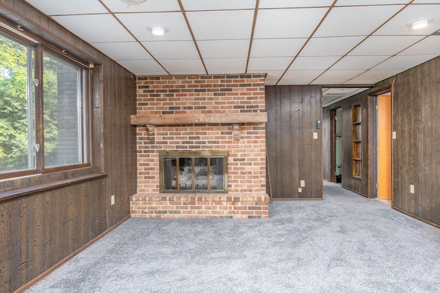 unfurnished living room featuring a fireplace, a paneled ceiling, carpet floors, and wooden walls