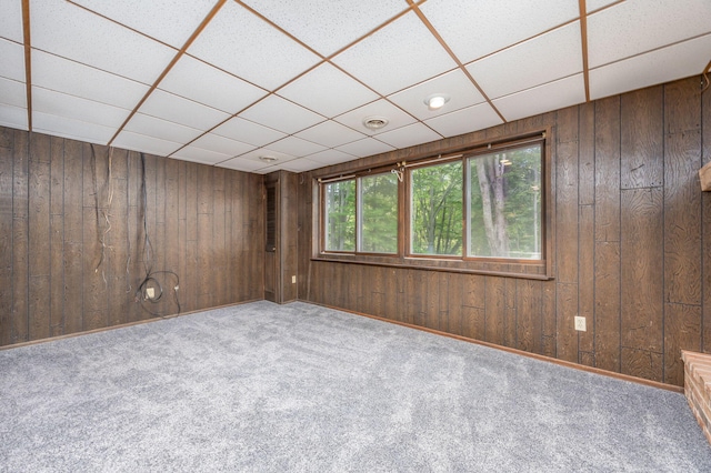 empty room featuring carpet flooring, a drop ceiling, and wooden walls