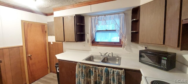 kitchen with ornamental molding, a textured ceiling, wooden walls, sink, and light hardwood / wood-style floors