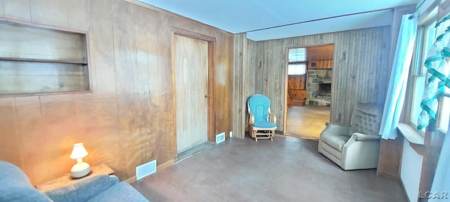 sitting room with concrete floors, a stone fireplace, and wooden walls