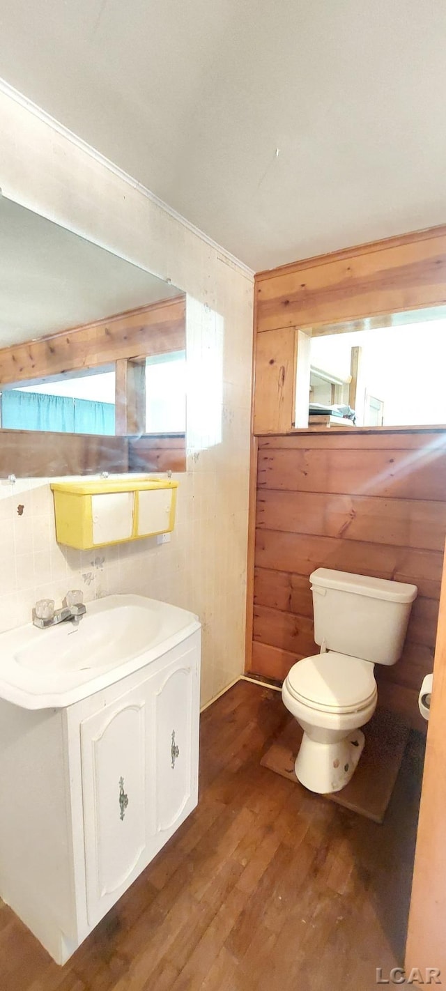 bathroom with hardwood / wood-style floors, vanity, toilet, and wooden walls