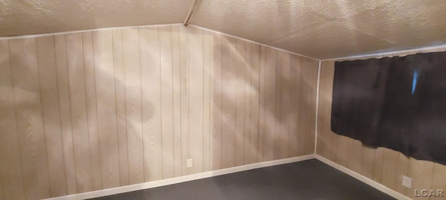 bonus room featuring a textured ceiling, wooden walls, and lofted ceiling