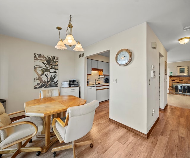 dining room with a brick fireplace, sink, and light hardwood / wood-style flooring