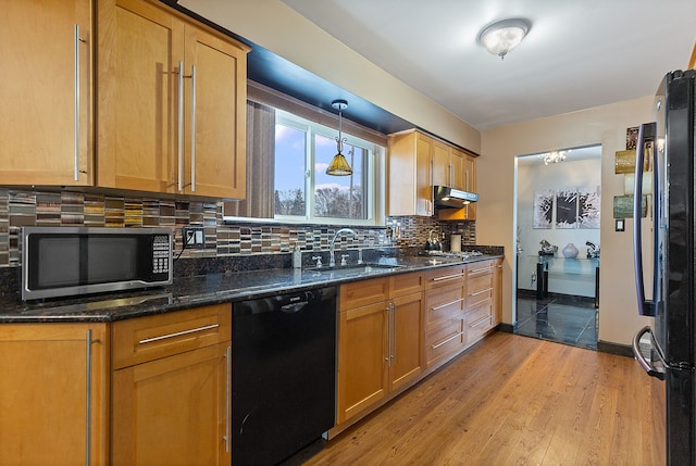 kitchen with dark stone countertops, black appliances, light wood-type flooring, sink, and decorative light fixtures