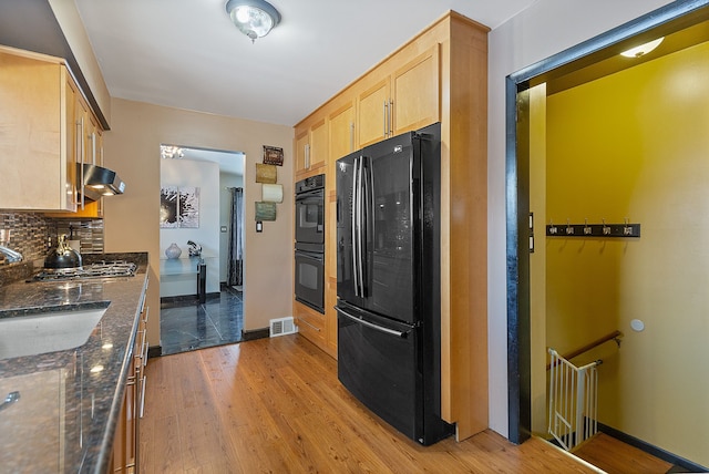 kitchen with dark stone countertops, black appliances, light wood-type flooring, light brown cabinetry, and tasteful backsplash