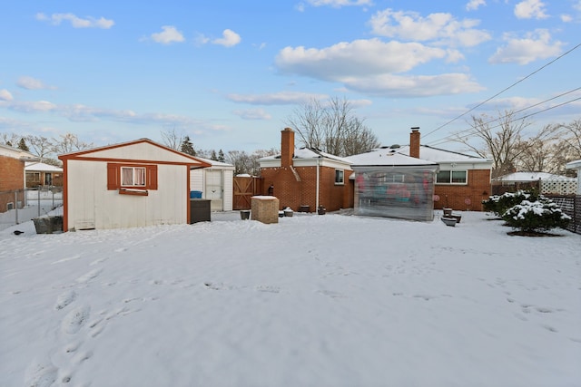 snow covered back of property featuring a storage unit