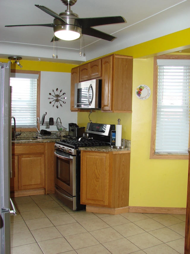 kitchen with ceiling fan, light tile patterned flooring, dark stone countertops, and appliances with stainless steel finishes