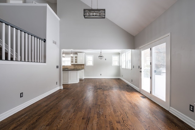 unfurnished living room with a notable chandelier, dark wood-type flooring, and high vaulted ceiling