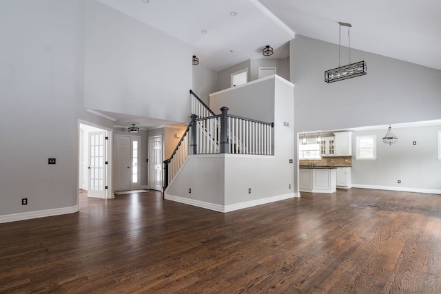 unfurnished living room with a notable chandelier, dark hardwood / wood-style flooring, and high vaulted ceiling