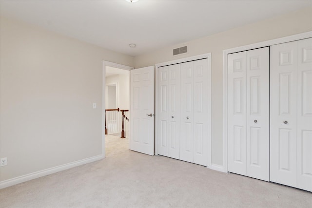 unfurnished bedroom with light colored carpet, visible vents, baseboards, and two closets