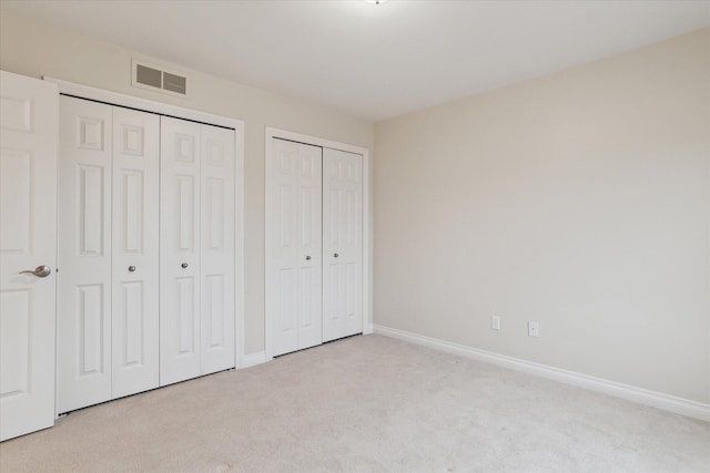 unfurnished bedroom featuring baseboards, visible vents, multiple closets, and carpet flooring