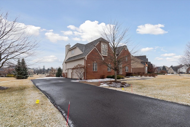 view of side of property with a chimney, aphalt driveway, and brick siding