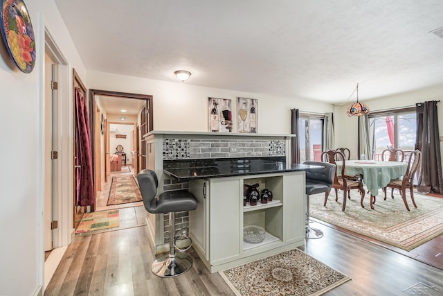 kitchen featuring decorative backsplash, a kitchen breakfast bar, decorative light fixtures, and light hardwood / wood-style flooring