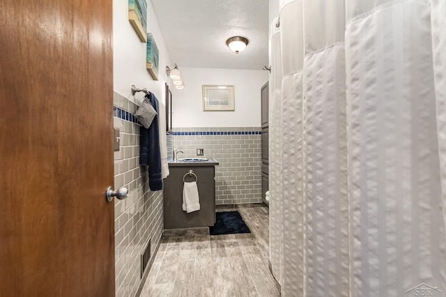 bathroom featuring sink, walk in shower, hardwood / wood-style floors, a textured ceiling, and tile walls