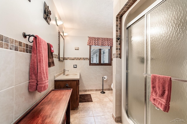 bathroom with a textured ceiling, vanity, an enclosed shower, and tile walls