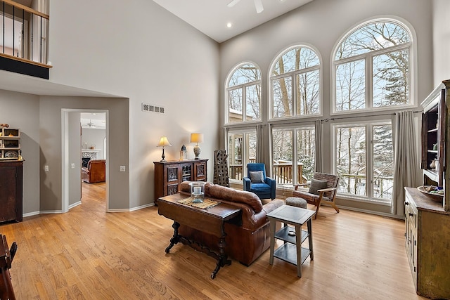 living room with ceiling fan, light hardwood / wood-style floors, and a high ceiling