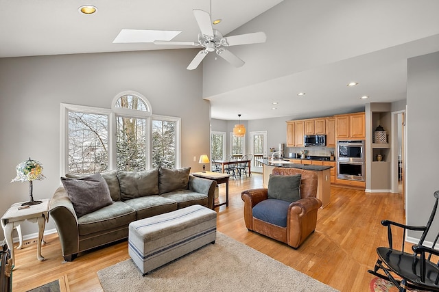 living room featuring a skylight, ceiling fan, high vaulted ceiling, and light wood-type flooring