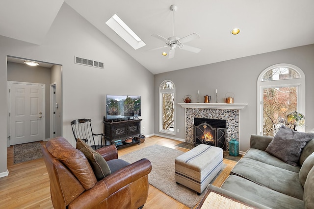 living room featuring a tile fireplace, light hardwood / wood-style floors, ceiling fan, and a healthy amount of sunlight