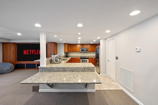 kitchen with kitchen peninsula, appliances with stainless steel finishes, decorative backsplash, a breakfast bar, and sink