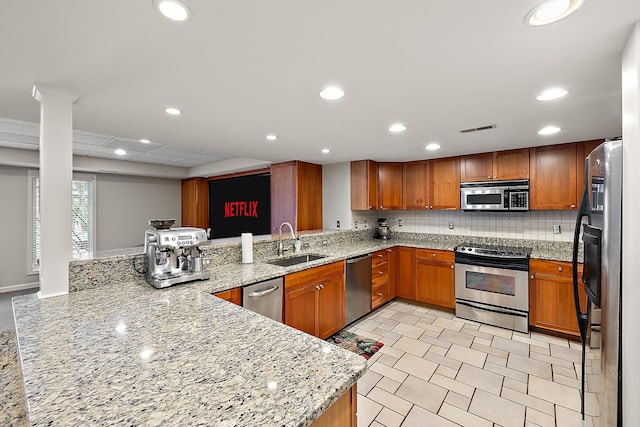 kitchen with sink, tasteful backsplash, light stone counters, kitchen peninsula, and appliances with stainless steel finishes