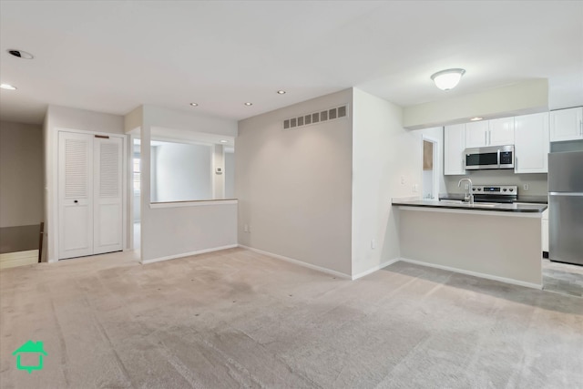 kitchen featuring kitchen peninsula, appliances with stainless steel finishes, light carpet, sink, and white cabinets