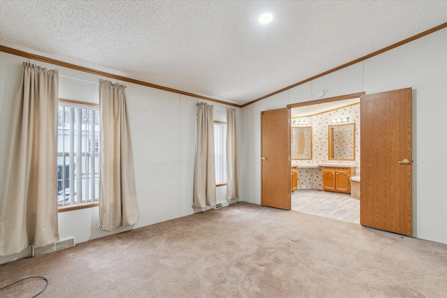 unfurnished bedroom with ensuite bath, ornamental molding, a textured ceiling, light colored carpet, and lofted ceiling