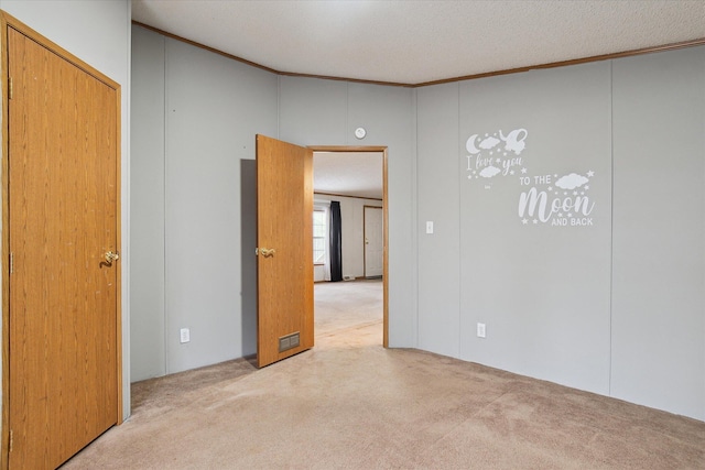 unfurnished room with light colored carpet, a textured ceiling, and ornamental molding