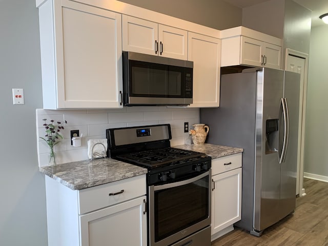 kitchen with tasteful backsplash, white cabinets, and stainless steel appliances