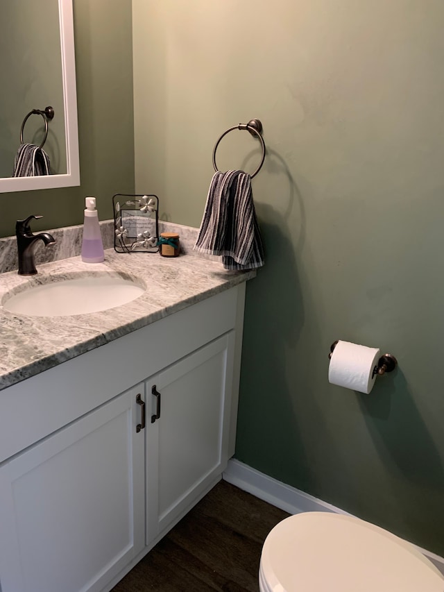 half bathroom with toilet, vanity, baseboards, and wood finished floors