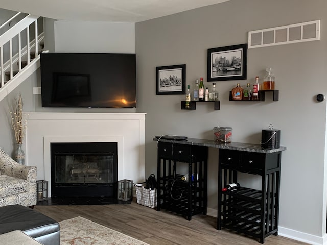 living room featuring a fireplace with flush hearth, wood finished floors, visible vents, and baseboards