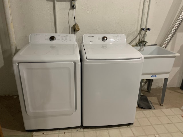 laundry area with laundry area, a textured wall, independent washer and dryer, and a sink