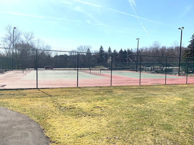 view of tennis court with a yard and fence