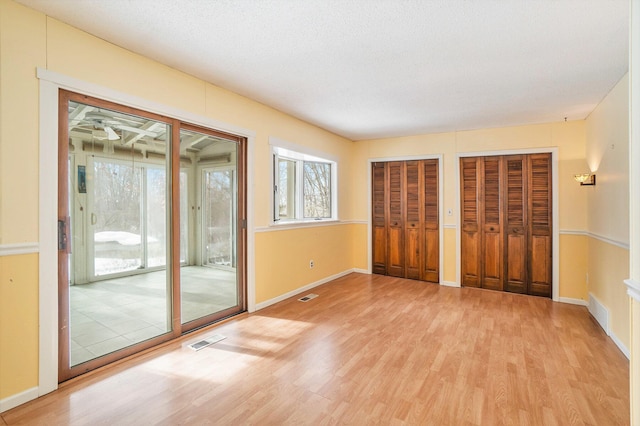 unfurnished bedroom with access to exterior, a textured ceiling, multiple closets, and light wood-type flooring