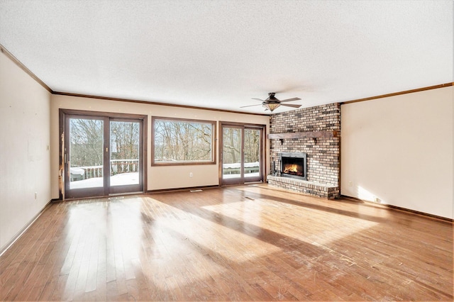 unfurnished living room featuring ceiling fan, light hardwood / wood-style floors, a brick fireplace, and a textured ceiling