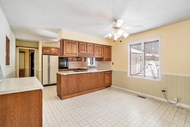 kitchen with white refrigerator, kitchen peninsula, black oven, and a textured ceiling